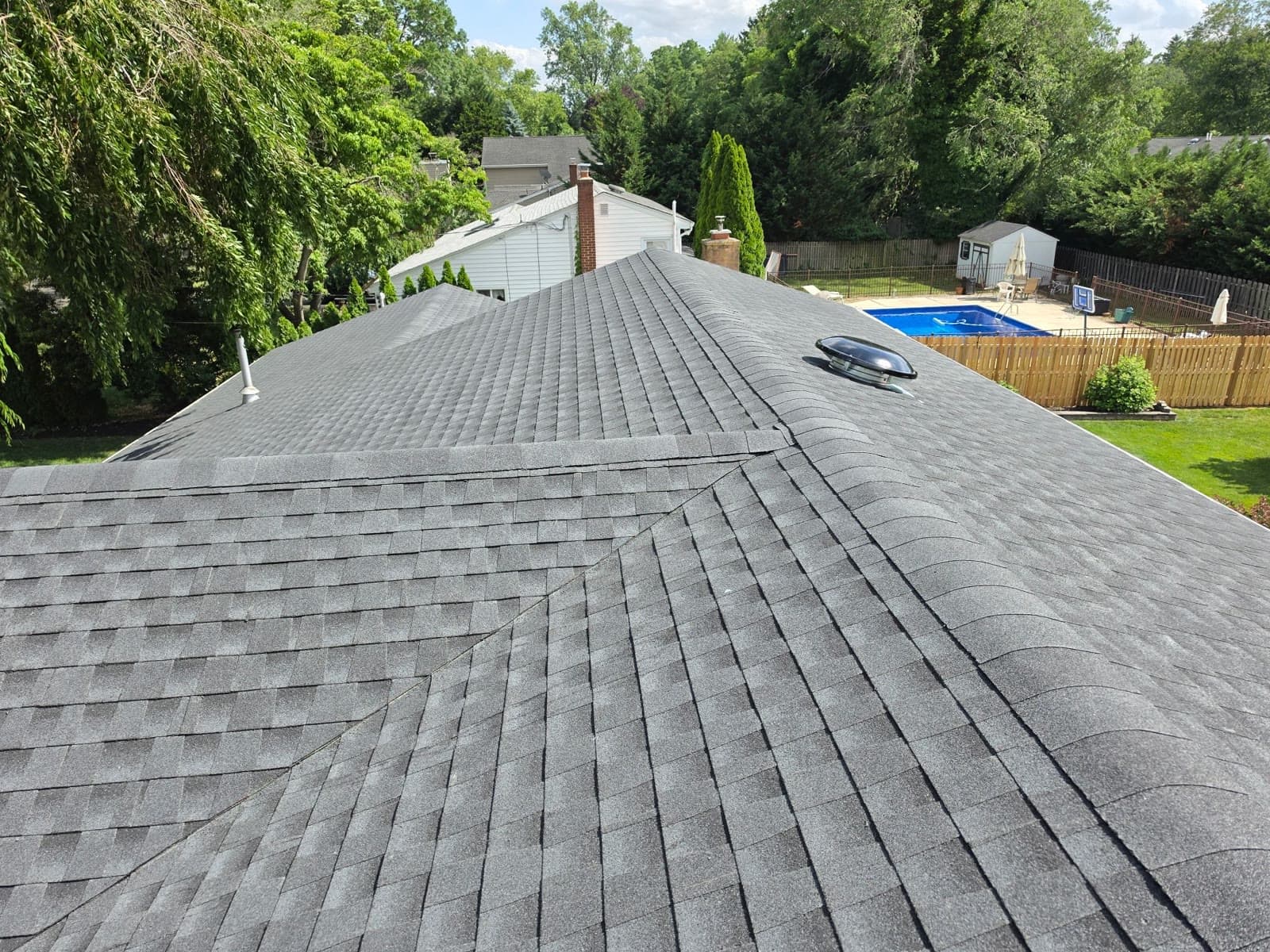 A finished gray roof with a skylight beside a pool yard — Green Apple Roofing, New Jersey