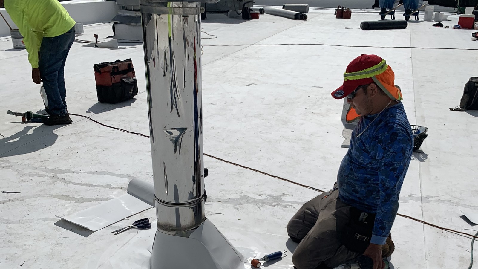 A Green Apple Roofing crew member sealing a pipe-penetration flashing on a white TPO commercial flat roof in New Jersey