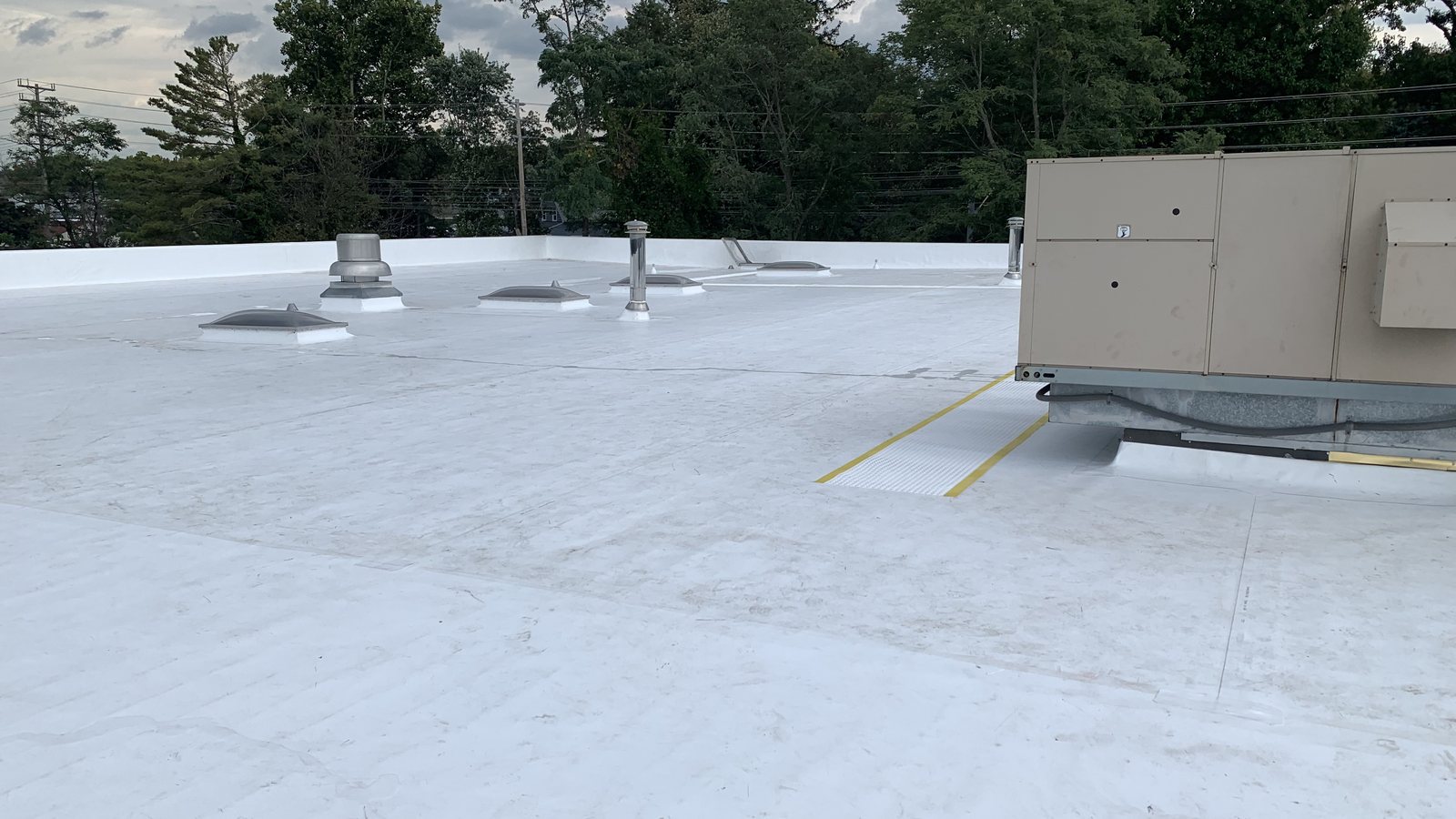 A finished white single-ply flat roof with a rooftop unit on its curb, yellow walkway lines, vents and skylight domes