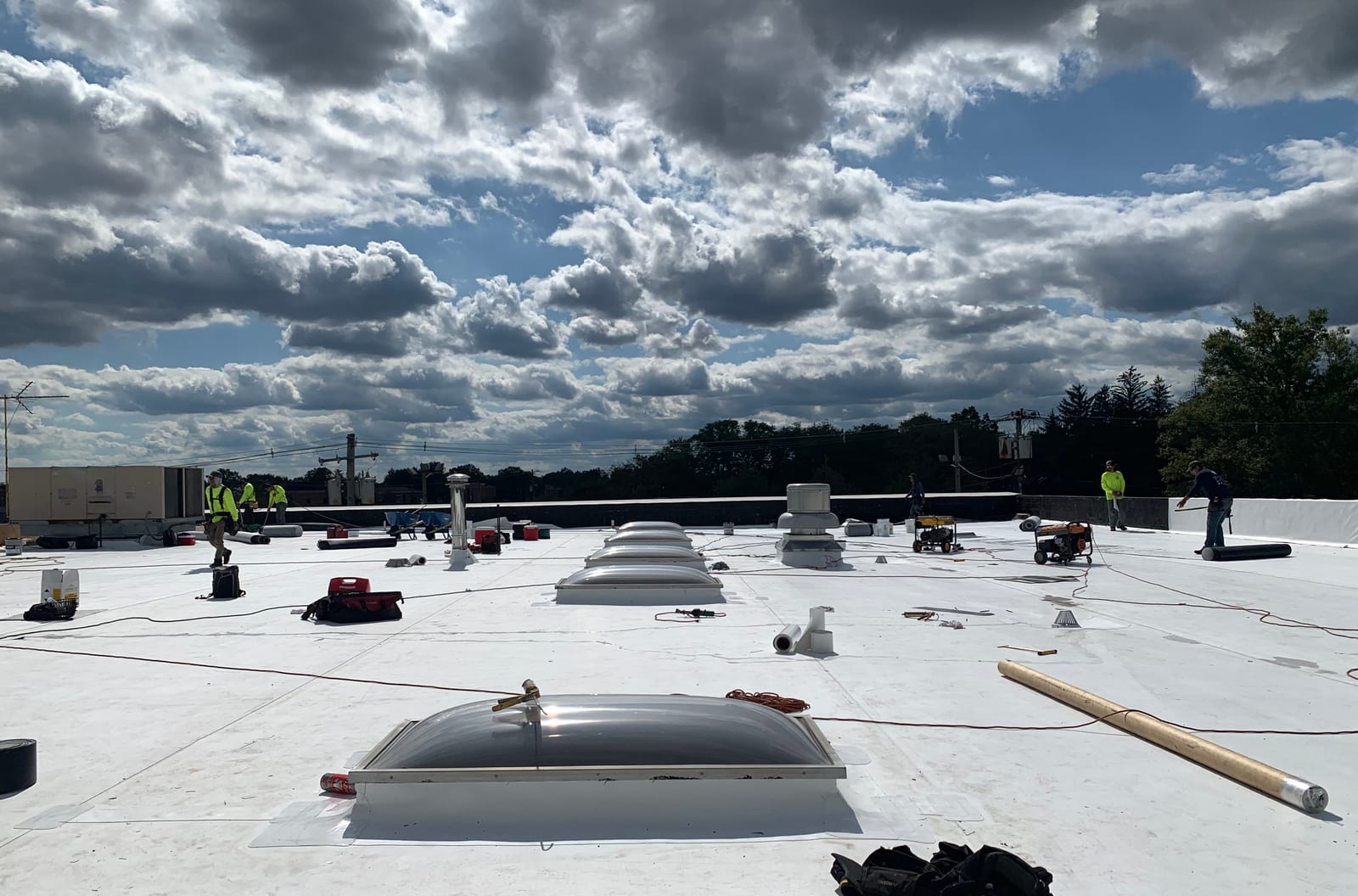 White single-ply membrane roof on a commercial building with skylight domes and rooftop units, small crew in the distance