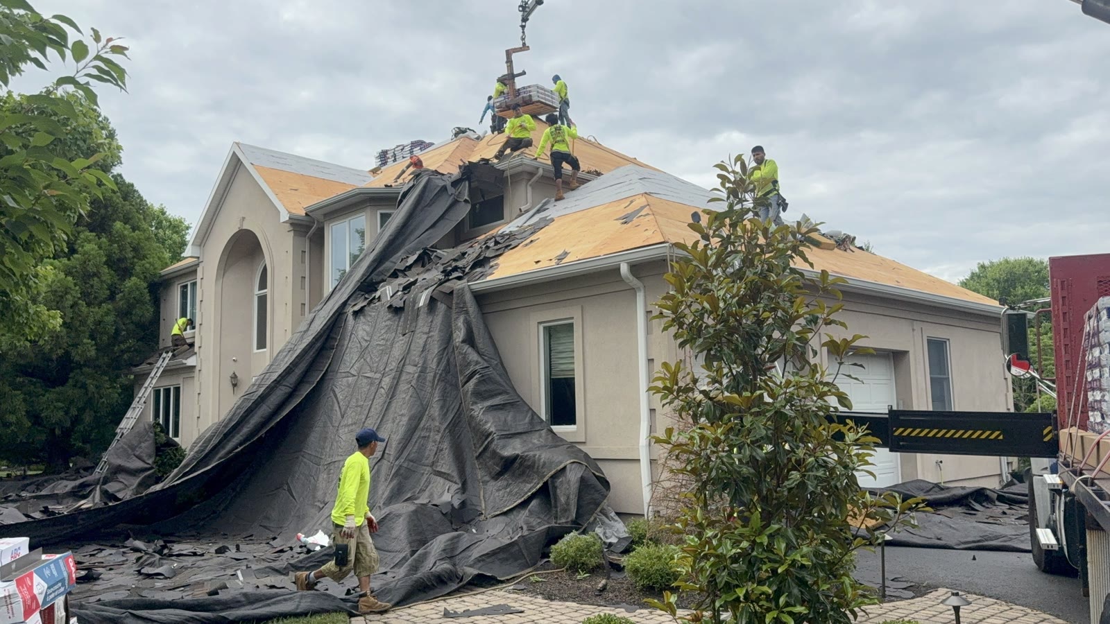 A full Green Apple Roofing crew with a crane and material truck re-roofing a large New Jersey home — a licensed, insured, professional operation