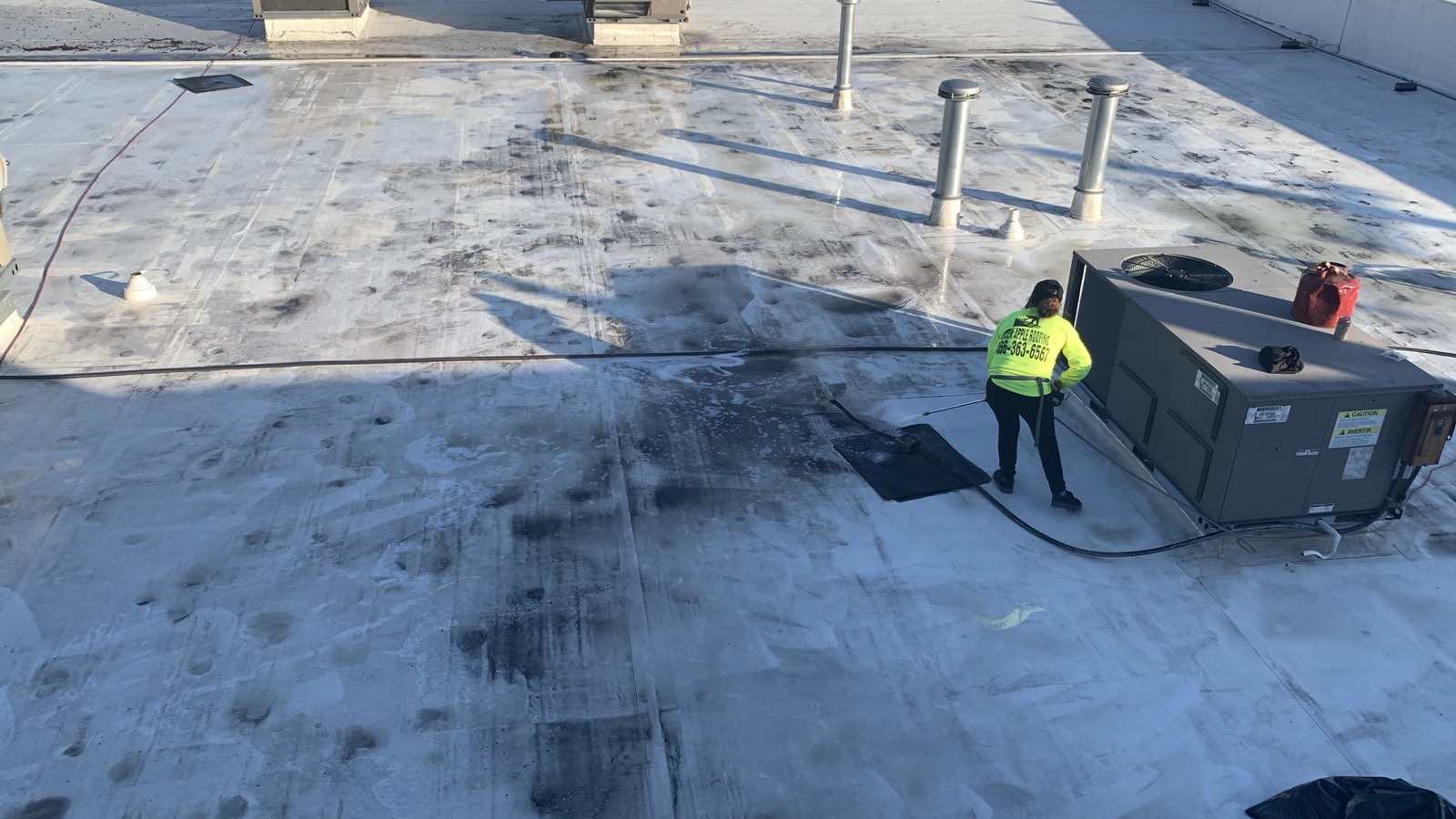 A New Jersey commercial flat roof showing dark staining where water repeatedly stands, with a rooftop HVAC unit and a Green Apple Roofing crew member working nearby