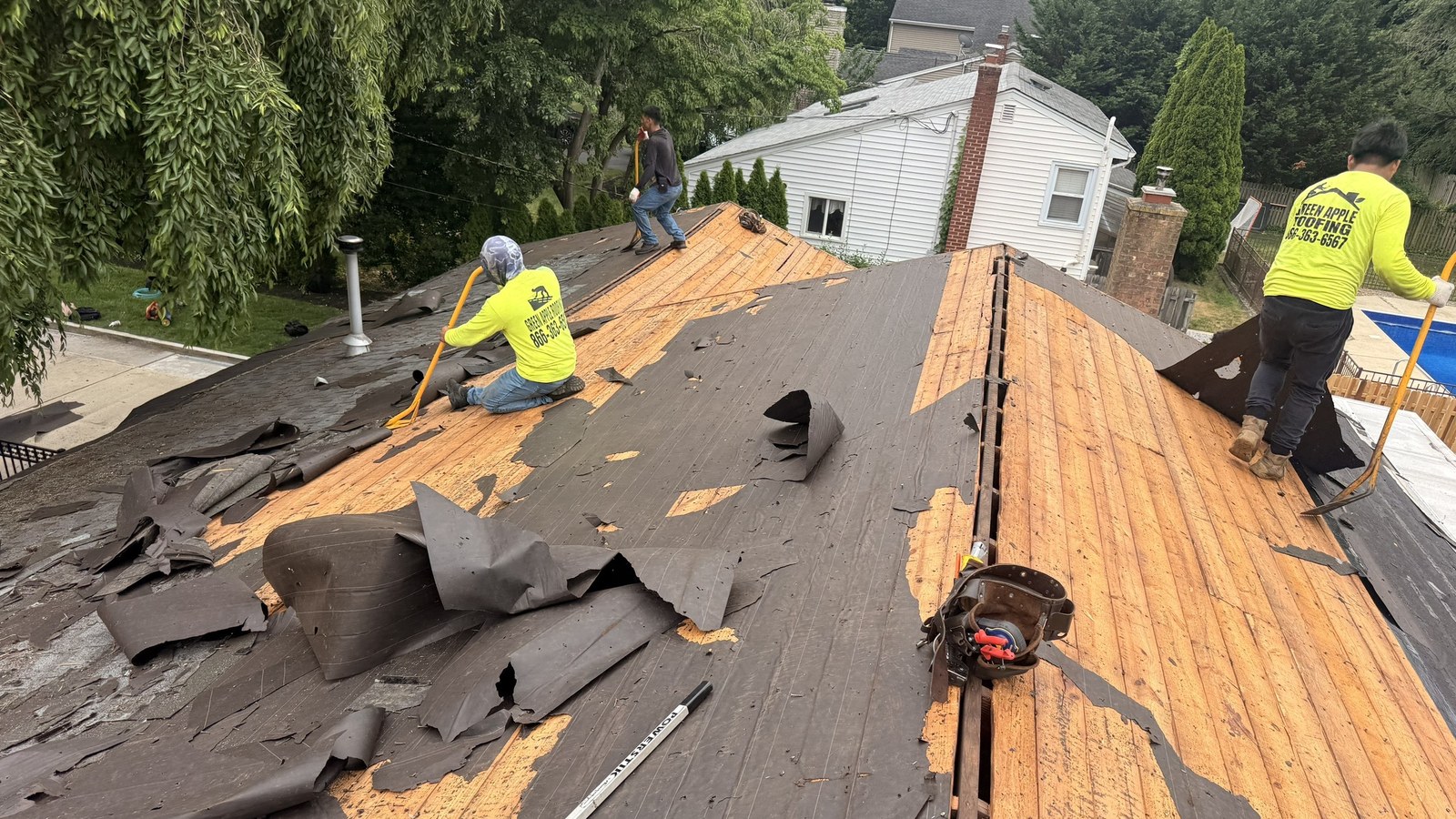 A Green Apple Roofing crew working on a New Jersey roof, stripping worn roofing down to the wood decking mid-project