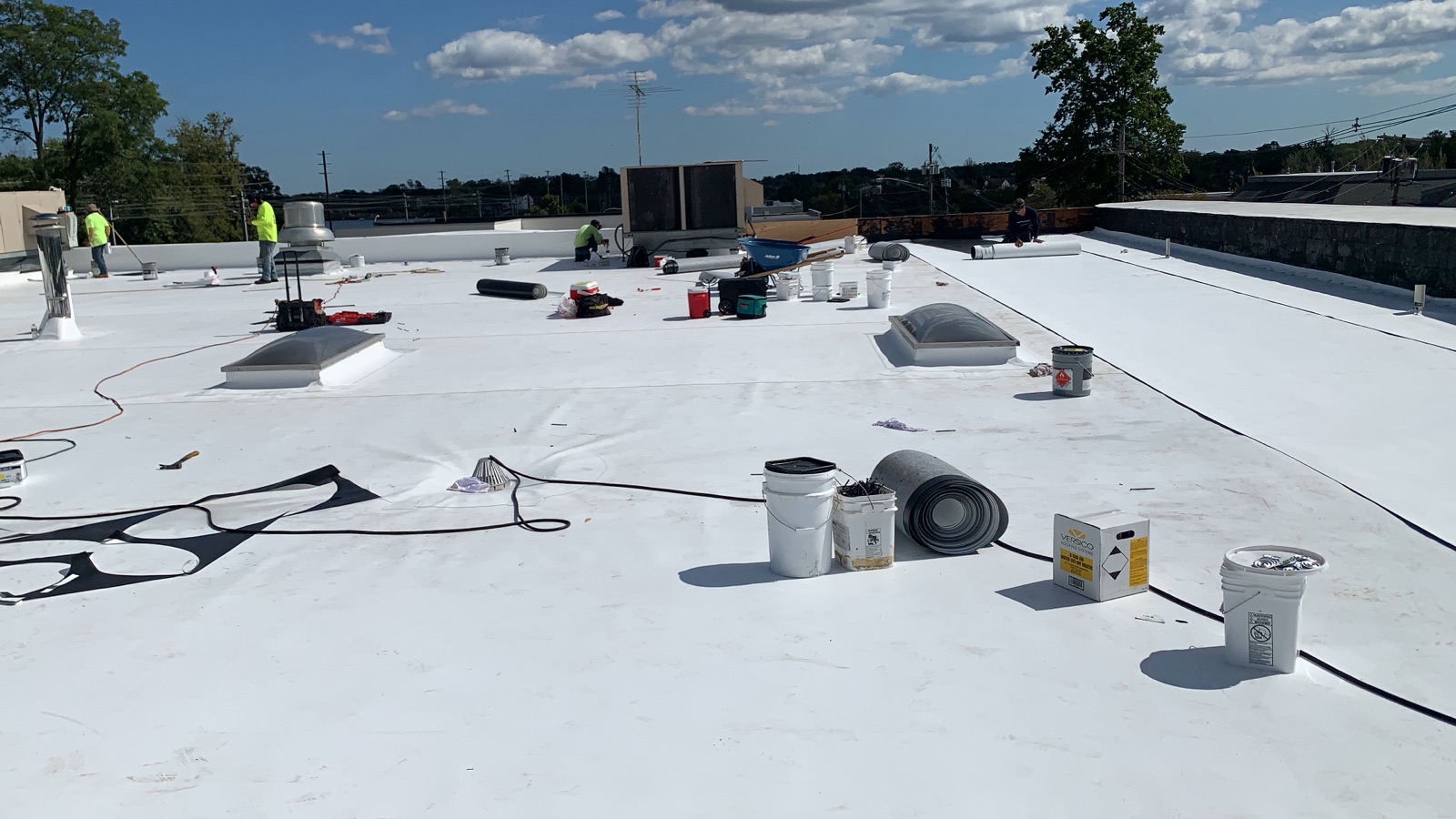 A newly installed white single-ply membrane covering a New Jersey commercial flat roof, with a Green Apple Roofing crew finishing details at the parapet