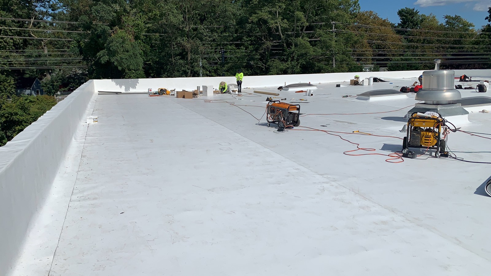 A large white TPO membrane roof on a New Jersey commercial building, with a Green Apple Roofing crew installing details in the background