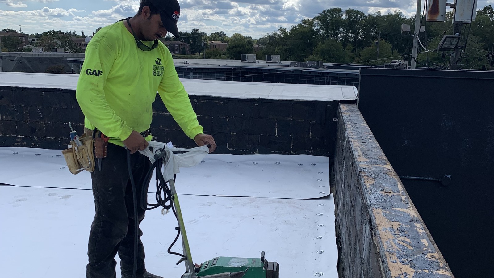 A Green Apple Roofing installer running a hot-air welder across a white TPO membrane on a New Jersey commercial flat roof
