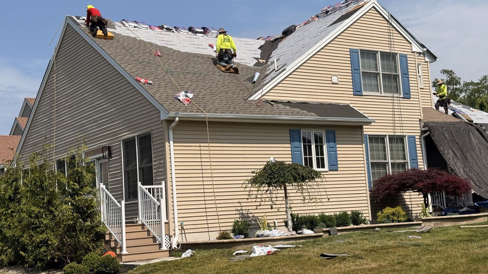 A Green Apple Roofing crew mid tear-off on a New Jersey home, with underlayment down on the front slope and shingle bundles staged along the ridge