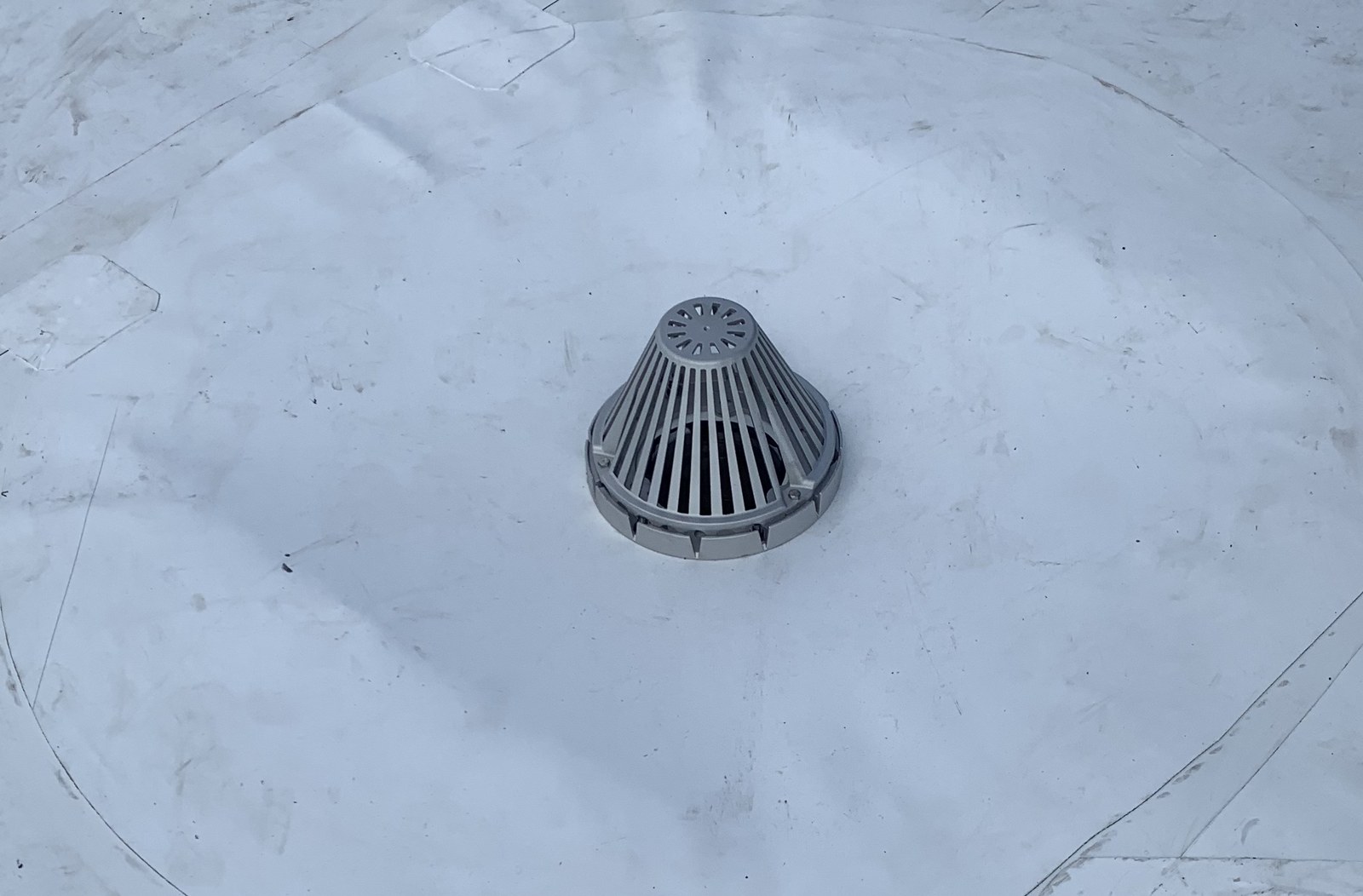 A roof drain's metal strainer dome on a white single-ply flat roof, with a welded membrane patch around it