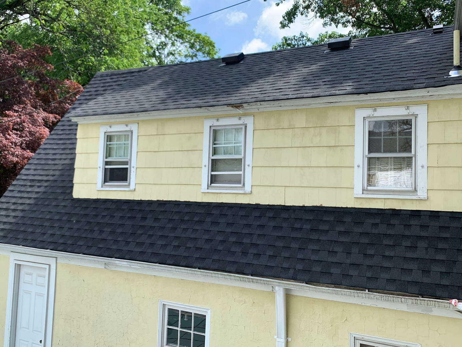 New black architectural shingles on a yellow-sided house, running down to the white gutter at the eave